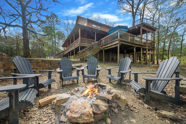 A cabin with a fire pit and Adirondack chairs.