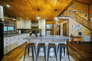 A spacious kitchen with a large island, wooden ceiling, and a staircase leading to a loft area.