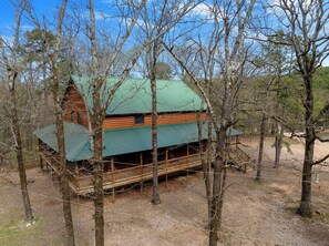 A log cabin with a green roof, surrounded by trees. - Cozy Cabin with Hot Tub and Game Loft (Broken Bow)