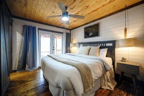 A bedroom with a wooden ceiling, a bed with white bedding, a nightstand, a wall-mounted lamp, and a ceiling fan.