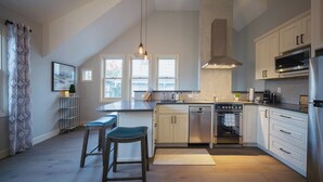 Et moderne køkken med en central ø, rustfrie hvidevarer og et stort vindue der giver naturligt lys.