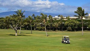 A golf course with a golf cart, palm trees, and a building in the background. - Top Flr, Kaanapali Golf Front, Beach Cabana, Jacuzzi (Kaanapali)