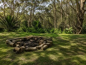 A natural outdoor setting with a fire pit surrounded by logs and a grassy area.