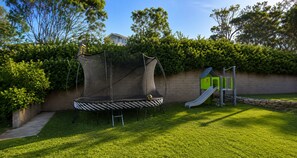 A backyard with a trampoline, a slide, and a playhouse.