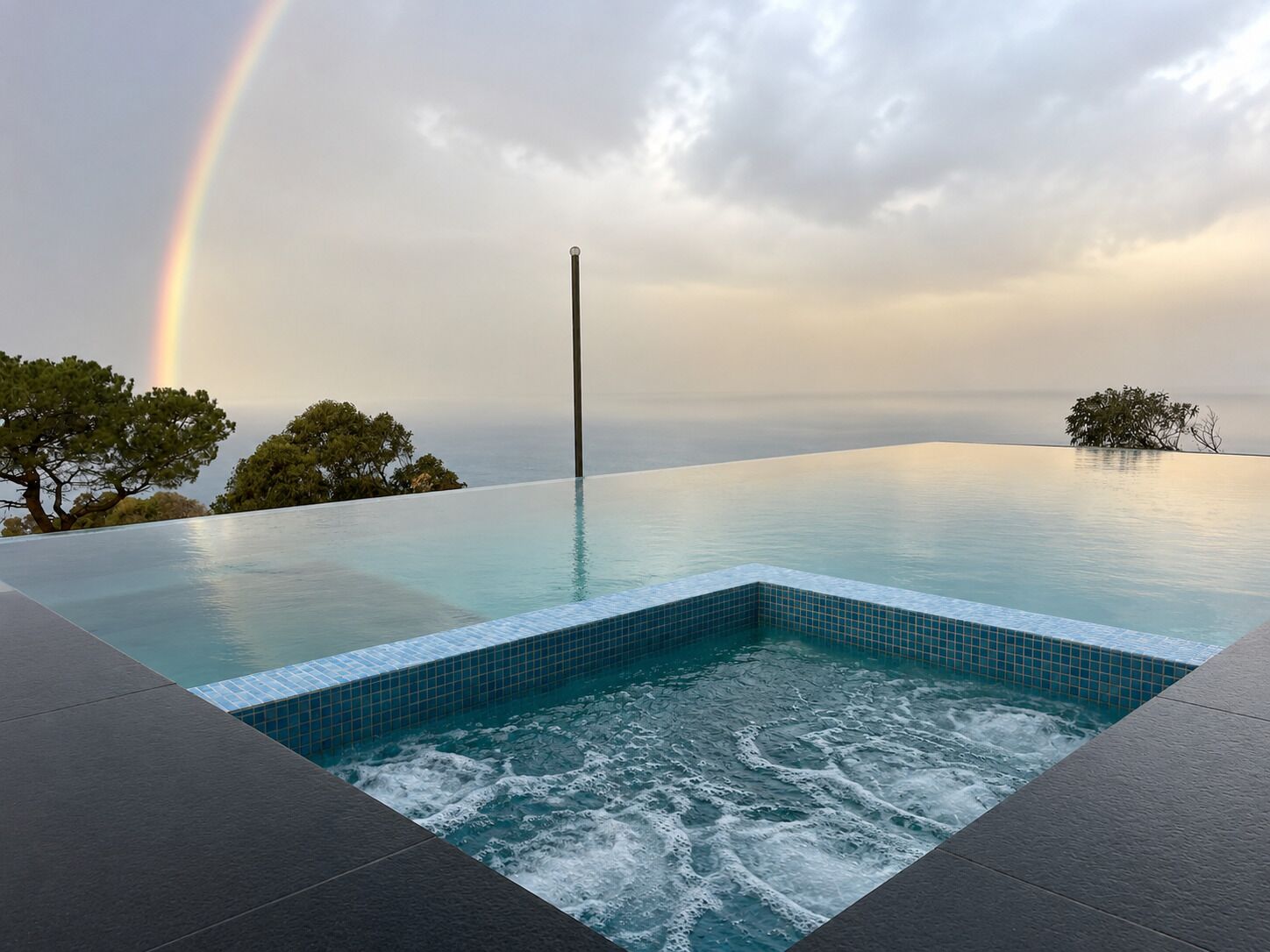 An infinity pool with a view of the sea and a rainbow.