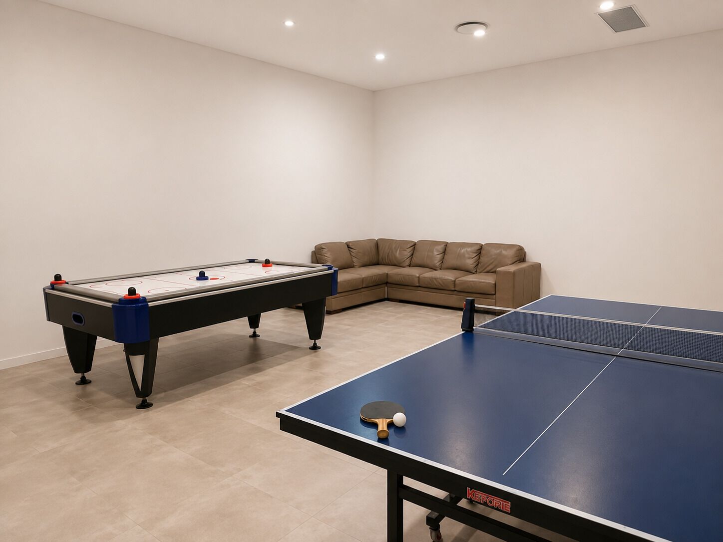 A room with a foosball table, a ping pong table, and a beige sofa.