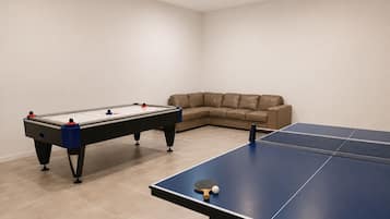 A room with a foosball table, a ping pong table, and a beige sofa.