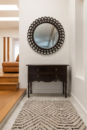 A dark wooden console table with drawers, a mirror with a circular frame, and a patterned rug on a wooden floor. - All The Views - Ocean & Bush with Heated Infinity Lap and Play Pool (Otford)