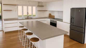 A modern kitchen with a central island, bar stools, a built-in oven, and a stainless steel refrigerator.