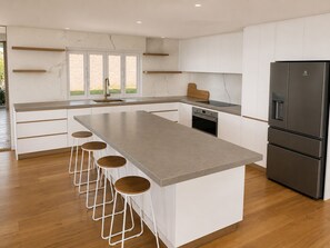 Una cocina moderna con una isla central, taburetes de bar, horno empotrado y refrigerador de acero inoxidable.
