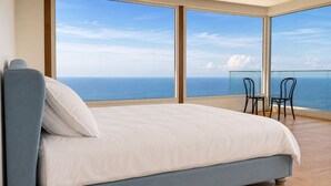 A bedroom with a large bed, a view of the ocean, and a balcony with chairs. - All The Views - Ocean & Bush with Heated Infinity Lap and Play Pool (Otford)