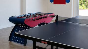 A room with a foosball table, a ping pong table, and a dartboard.