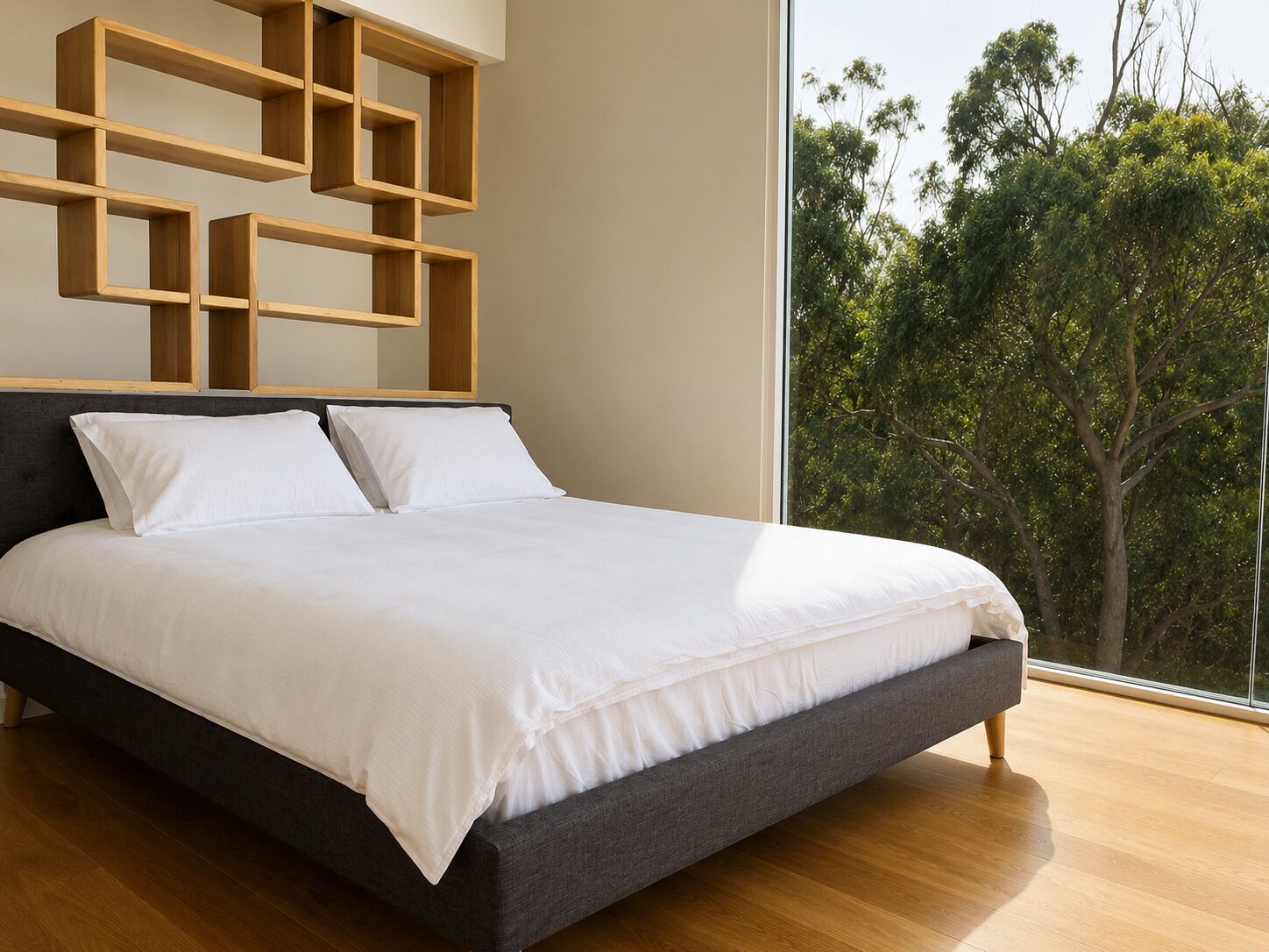 A modern bedroom with a large bed, a dark headboard, and a view of trees through a large window.