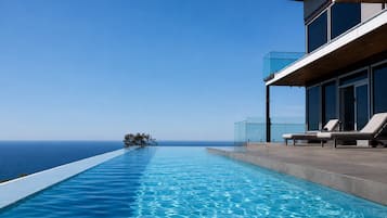 A modern infinity pool with clear blue water, a wooden deck, and a view of the ocean.