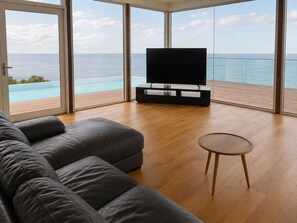 A modern living room with a large flat-screen TV, a leather sofa, and a small wooden table.
