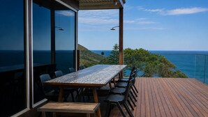A wooden deck with a table and chairs, overlooking a coastal landscape. - All The Views - Ocean & Bush with Heated Infinity Lap and Play Pool (Otford)