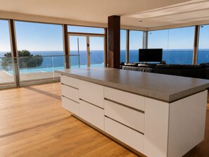 Una cocina moderna con una isla grande, suelo de madera y vistas al océano a través de amplios ventanales.