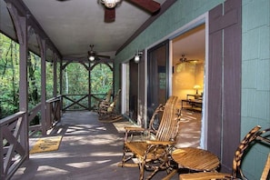 A covered porch with wooden chairs, a ceiling fan, and a view of the interior.
