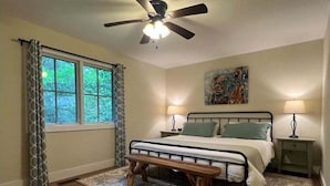 A bedroom with a bed, bedside tables, a ceiling fan, a window with curtains, and a rug. - Shady Creek Cabin in Connestee Falls with stream (Brevard)