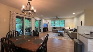 A spacious living area with a dining table, sofas, a TV, and a ceiling fan. - Shady Creek Cabin in Connestee Falls with stream (Brevard)