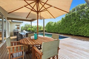 An outdoor deck with a wooden table and chairs, a large umbrella, and a swimming pool. - Bella Casa Sorrento (Sorrento)