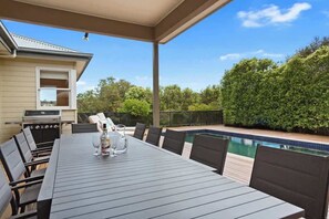 Eine Außenpatio mit Esstisch, Stühlen, einem Grill und einem Swimmingpool.