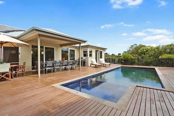 A swimming pool with a wooden deck, outdoor furniture, and a covered patio area.