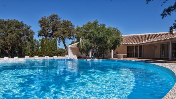 A clear blue swimming pool surrounded by trees and a building with a tiled roof. - An architectural gem in Las Tablas de Daimiel (Daimiel)
