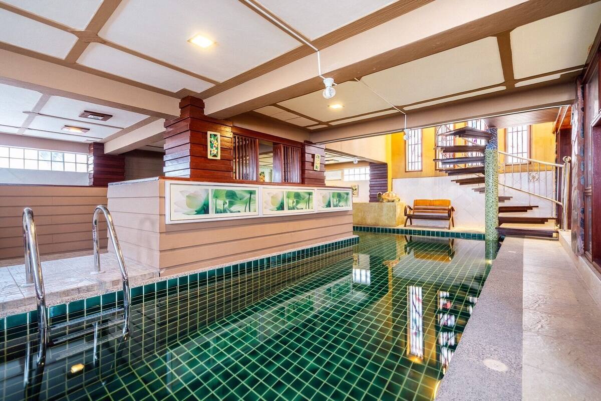 An indoor swimming pool with a tiled floor, a wooden bench, and a staircase leading to an upper level.