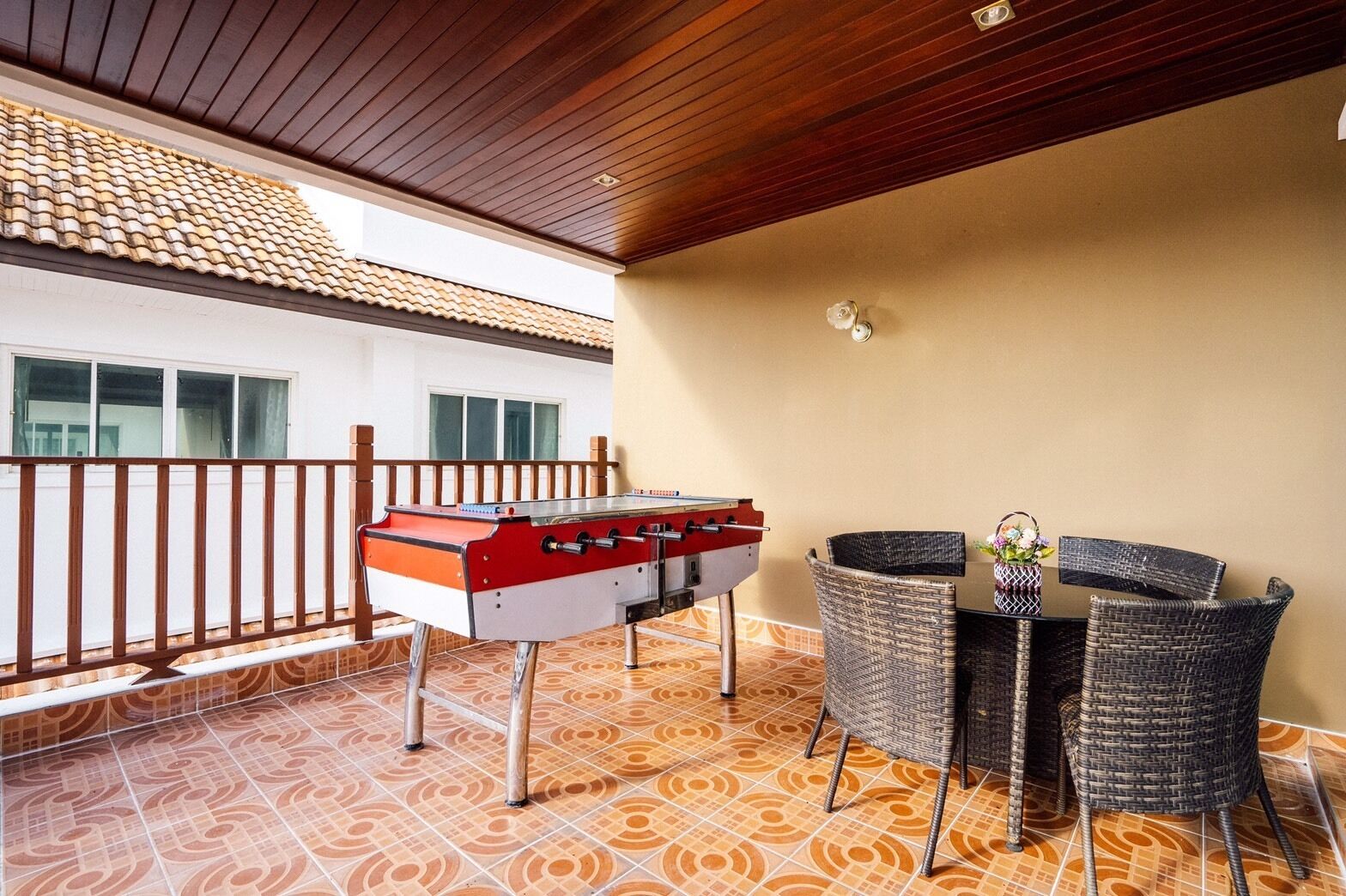 Un balcon avec une table de baby-foot, des fauteuils en osier et une petite table sur laquelle est posé un vase.