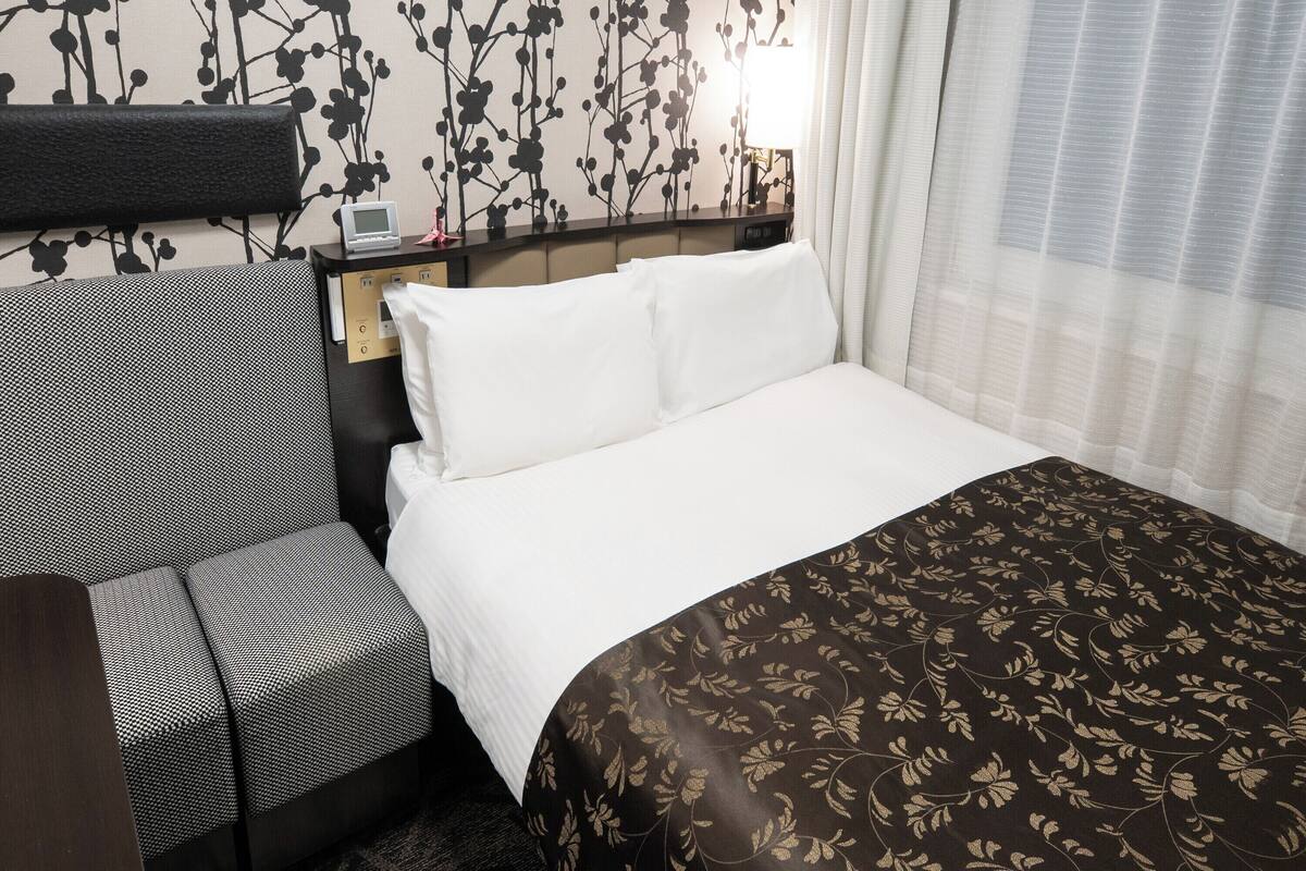 Hotelkamer met een bed, een bureau, een stoel en een muur met een zwart-wit bloemenpatroon.