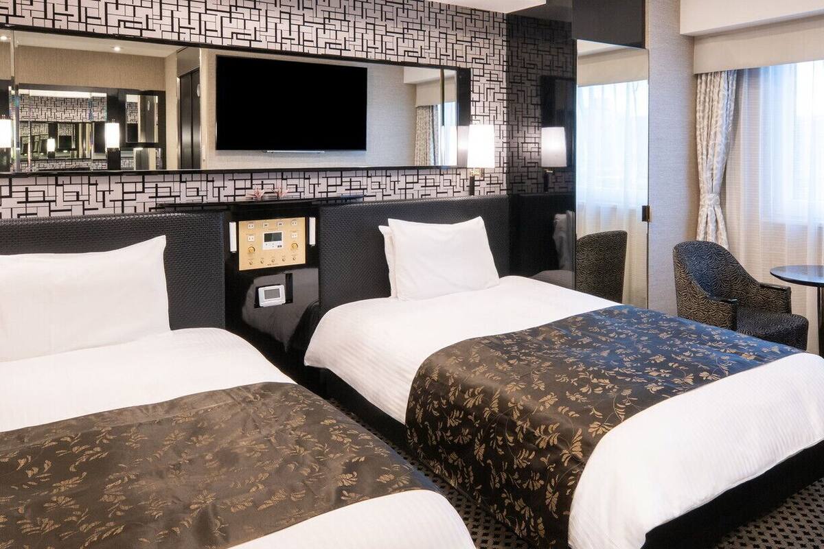 Een hotelkamer met twee bedden, een televisie, een bedieningspaneel, een klein tafeltje en een stoel.