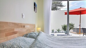 A hotel room with a bed, a wooden headboard, a window with a view of the outdoors, and a red umbrella outside. - Villa le Nid Des Dunes & Spa-1 Front de Mer (Santec)