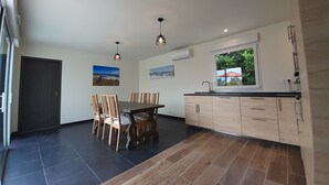 A modern kitchen with a dining area, featuring a large window, wooden cabinets, and a tiled floor. - Villa le Nid Des Dunes & Spa-1 Front de Mer (Santec)