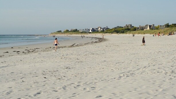 A wide sandy beach with a few people walking and standing. There are houses in the background along the shoreline. - Villa le Nid Des Dunes & Spa-1 Front de Mer (Santec)