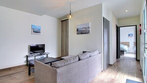 A modern living room with a grey sofa, a TV on a stand, and artwork on the walls. - Villa le Nid Des Dunes & Spa-1 Front de Mer (Santec)