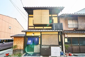 A traditional Japanese building with a wooden exterior, a small wooden structure to the left, and a sign with Japanese characters.
