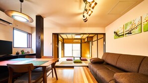 Un salón japonés tradicional con suelo de tatami, una mesa de madera baja, un sofá y una puerta corrediza que da a otra habitación.