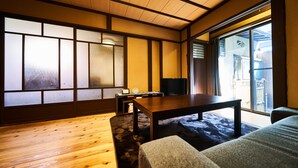 Una habitación japonesa tradicional con suelo de tatami, una mesa de madera baja, un sofá y una puerta corrediza de vidrio que da a un balcón.
