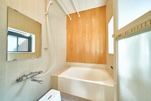 A modern bathroom with a wooden panel wall, a large bathtub, a mirror, and a shower area.