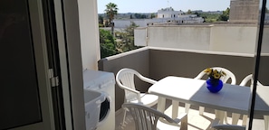 A balcony with a washing machine, white plastic chairs, a table, and a vase with flowers. - Appartamenti Rivabella Gallipoli (Gallipoli)