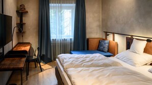 Hotellihuone, jossa on sänky, työpöytä, tuoli, televisio ja ikkuna, jossa on verhot.