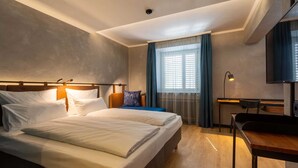 Ein Hotelzimmer mit Bett, Schreibtisch, Stuhl, Fernseher und einem Fenster mit Vorhängen.