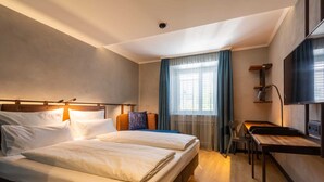 A hotel room with two beds, a desk, a TV, and a window with curtains.