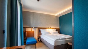 Moderni hotellihuone, jossa on suuri sänky, yöpöytä, tuoli ja pieni työpöytä.