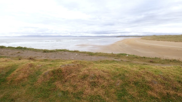 Eine Küstenlandschaft mit Sandstrand und einer grasbewachsenen Fläche.