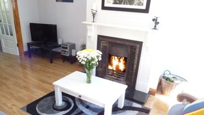 Ein Wohnzimmer mit weißem Couchtisch, Kamin und Fernseher.