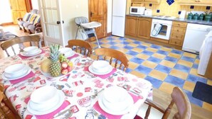 Ein Essbereich mit Tisch für vier Personen, Stühle, eine Küche mit Holzausstattung, einem Kühlschrank und einer Mikrowelle.