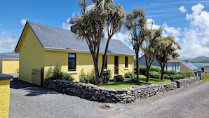 A yellow house with a stone wall and a gravel driveway. - Kate's Cottage (Valentia Island)