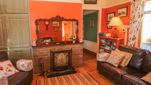 A living room with a fireplace, a sofa, a coffee table, and a bookshelf. - Kate's Cottage (Valentia Island)